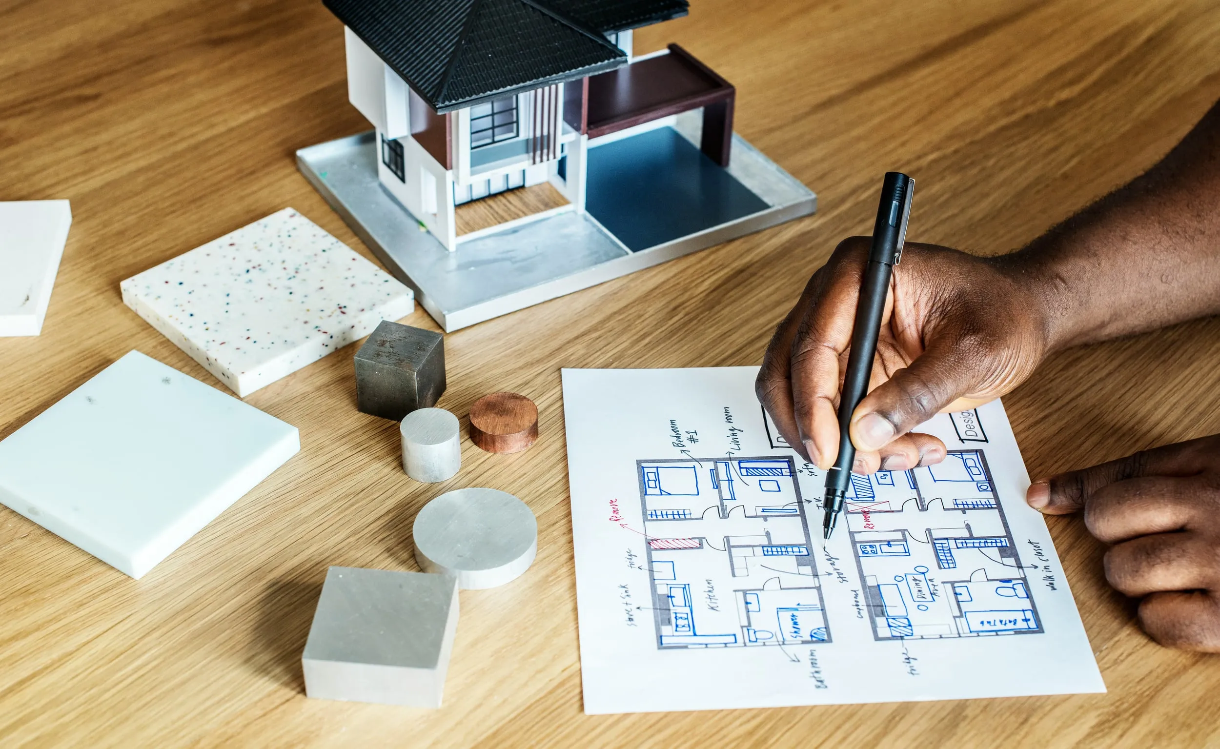 Mano disegna planimetria con modello casa e campioni materiali