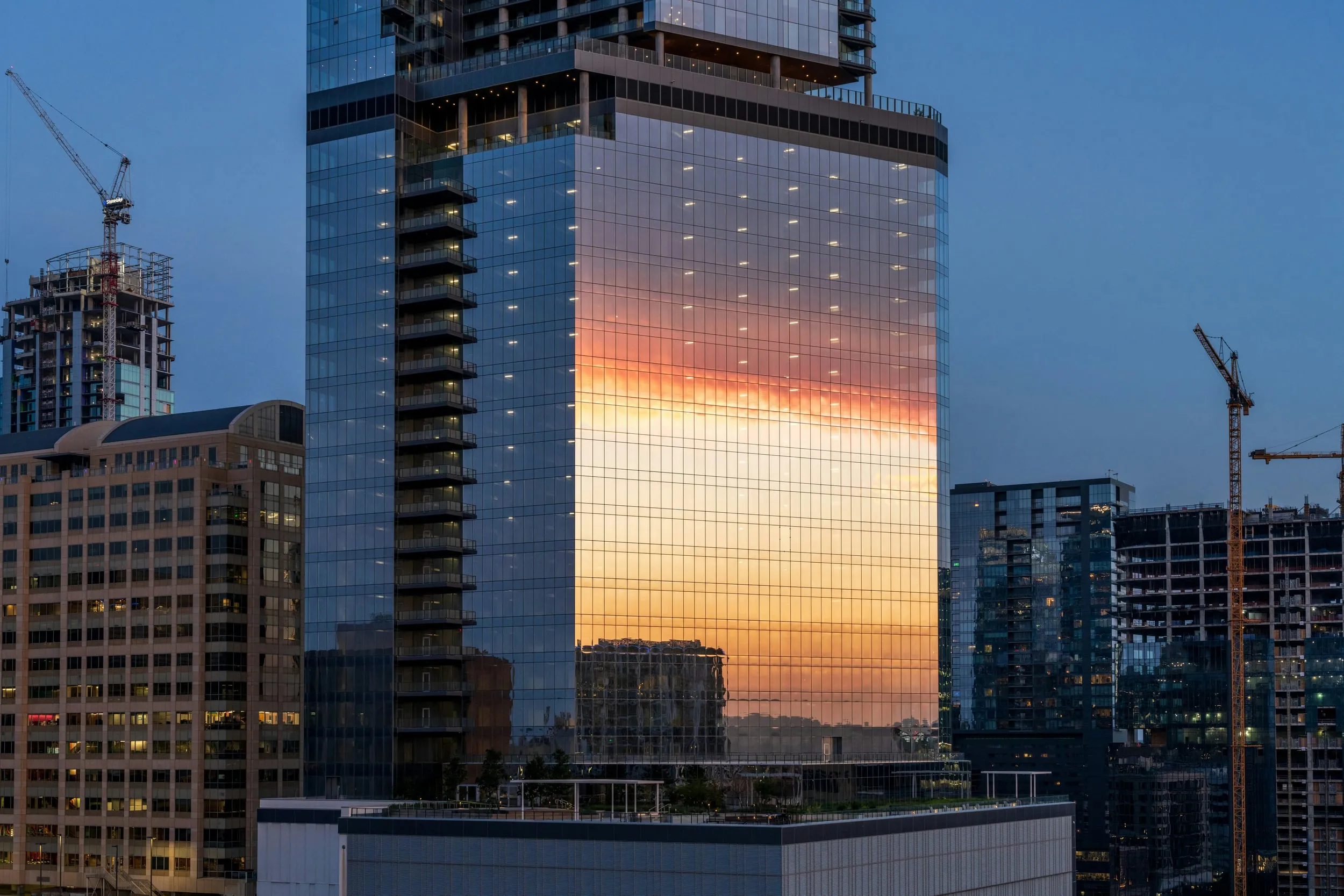 Grattacielo vetrato con tramonto riflesso e gru